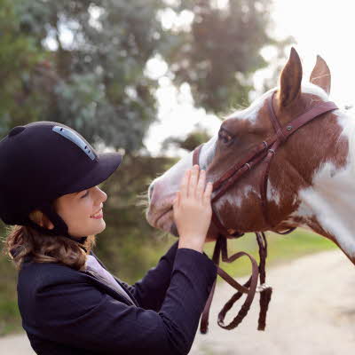 Jente i hestehjelm klapper en hest
