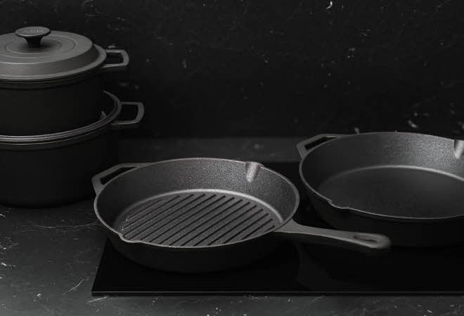 Sett med svart støpejernsgryter og stekepanner på mørk benkeplate.