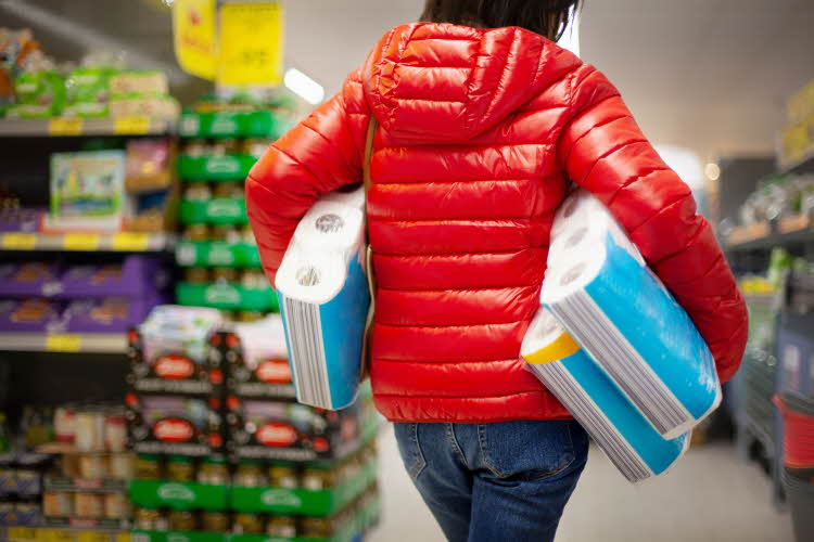Person i rød jakke inne på kjøpesenter med tre pakker toalettpapir under armene.
