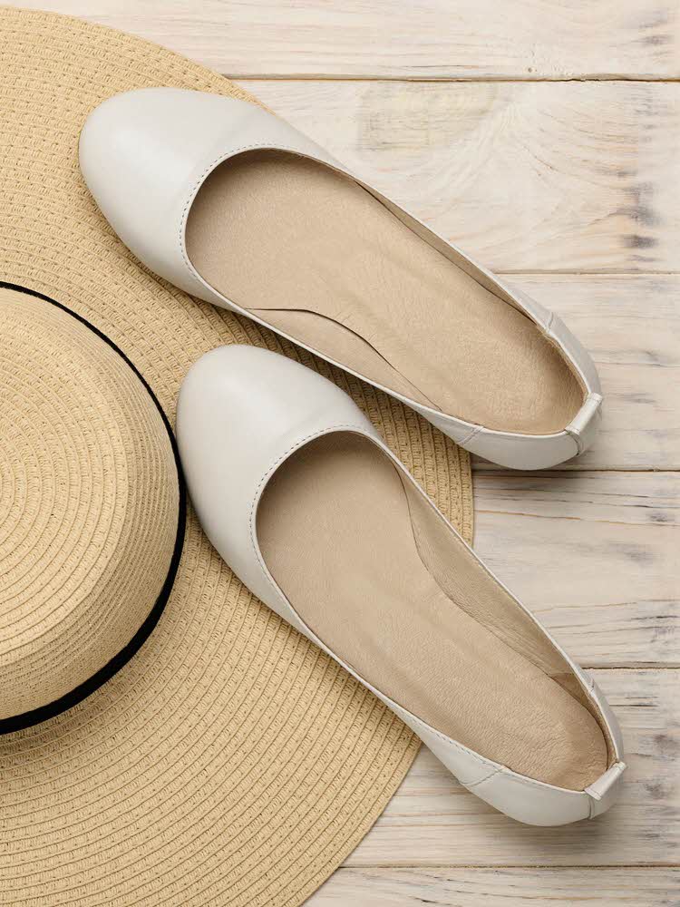 Et par hvite ballerinasko som ligger ved siden av en strå hatt