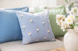 Tre pynteputer i blå og grønn på en sofa, med en vase med blomster i forgrunnen