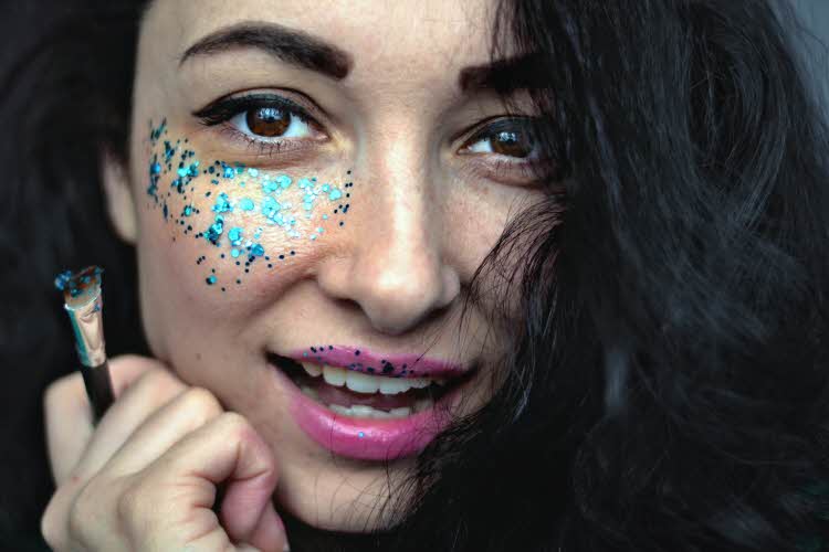 Jente holder sminkekost og har dekorativ blå glittersminke under øyet