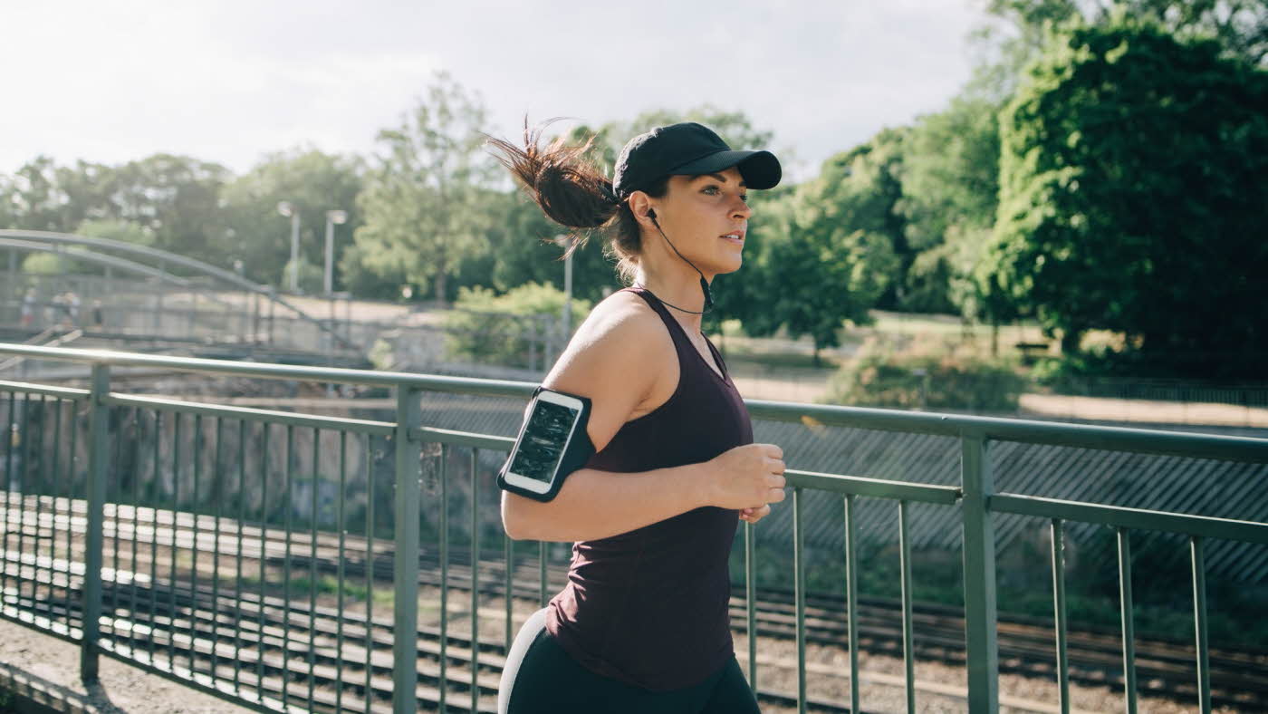 Dame løper i singlet, treningstights og caps med iphone på armen