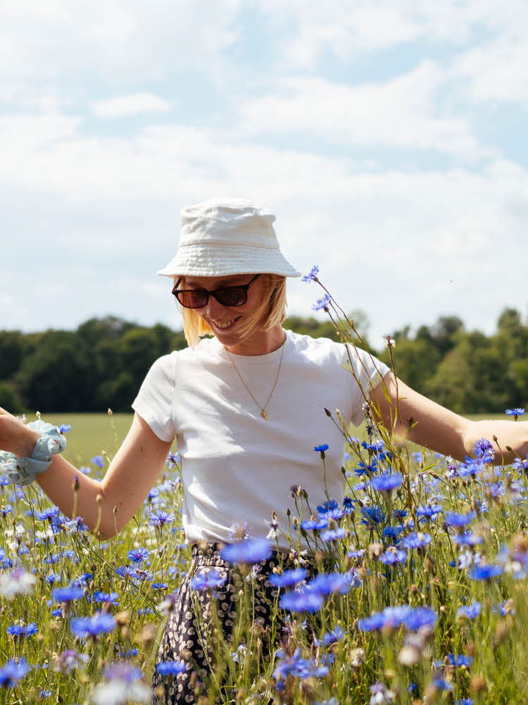 Smilende dame med hvit bøttehatt i blomstereng