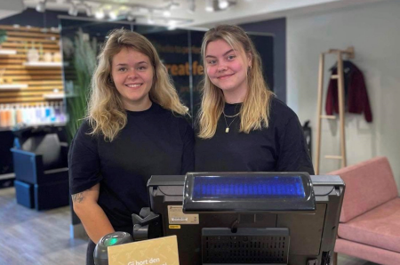 To-unge-smilende-damer-i-sorte-klær-som-står-ved-kassen-i-butikken