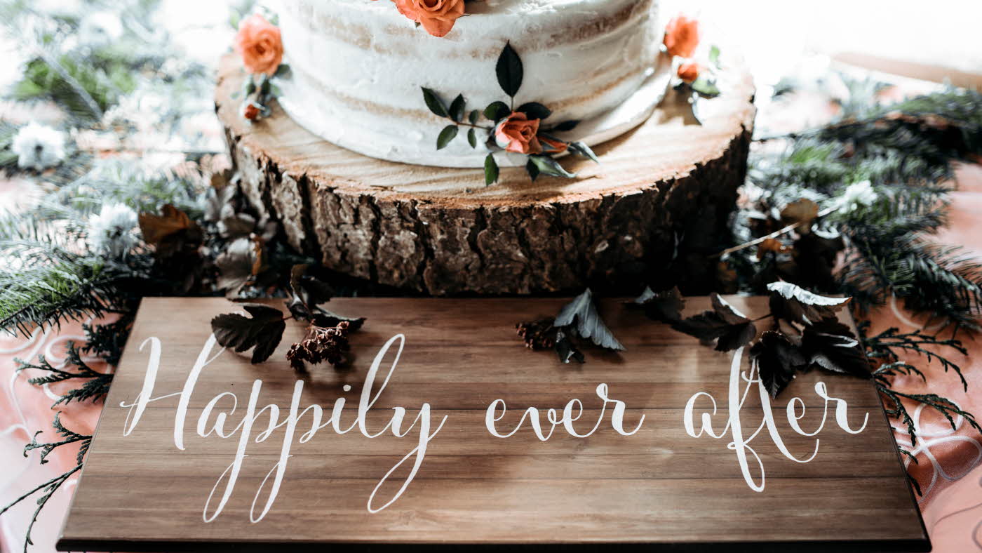 Hvit bryllupskake på treplanke hvor det står "happily ever after"
