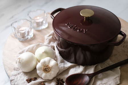 En støpejernsgryte fra Sabor som står på en kjøkkenbenk med hvitløk ved siden av.