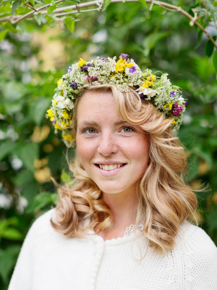 Blond jente smiler til kamera med blomsterkrans på hodet