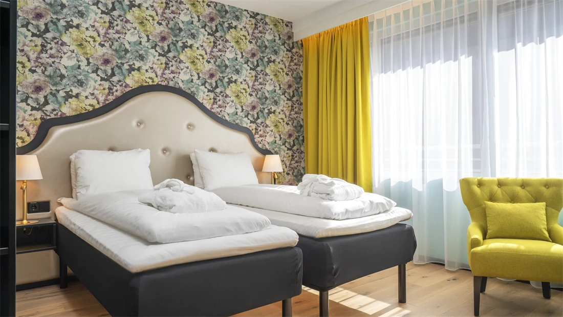 Separate senger med morgenkåper, blomstrete tapet, gule gardiner og store vinduer, gul stol i superior rom på Thon Hotel Cecil.