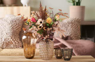 En vase med silkeblomster som står på et stuebord foran en sofa