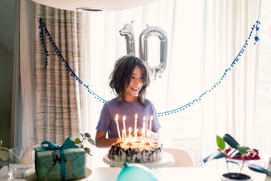 Gutt står i rom med kake, gaver og ballonger som viser tallet 10