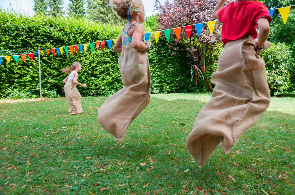 Barn leker sekkeløp i en hage dekorert med fargerike vimpler