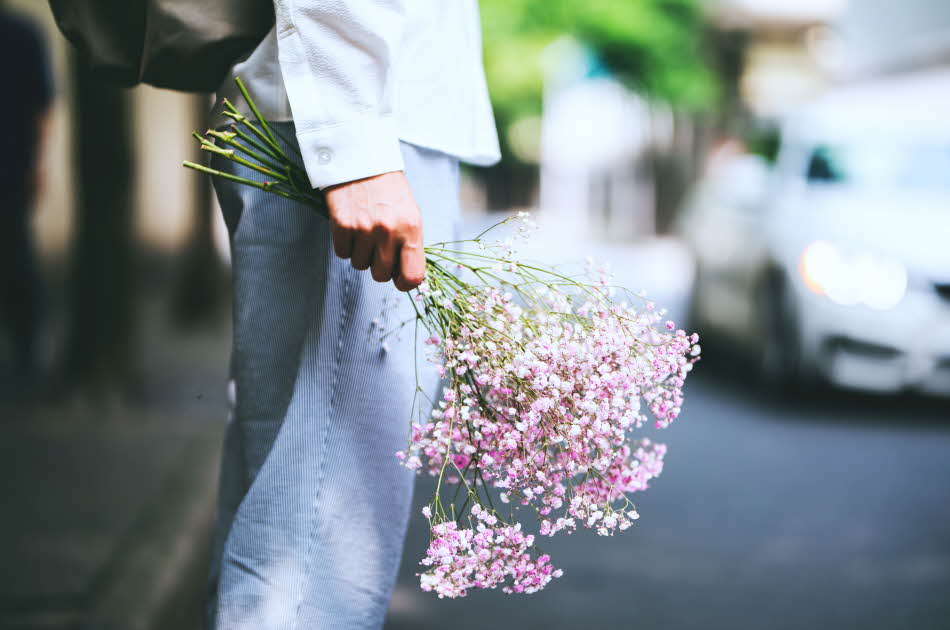 Nærbilde av hånd som holder en bukett blomster nedover låret, sett fra siden