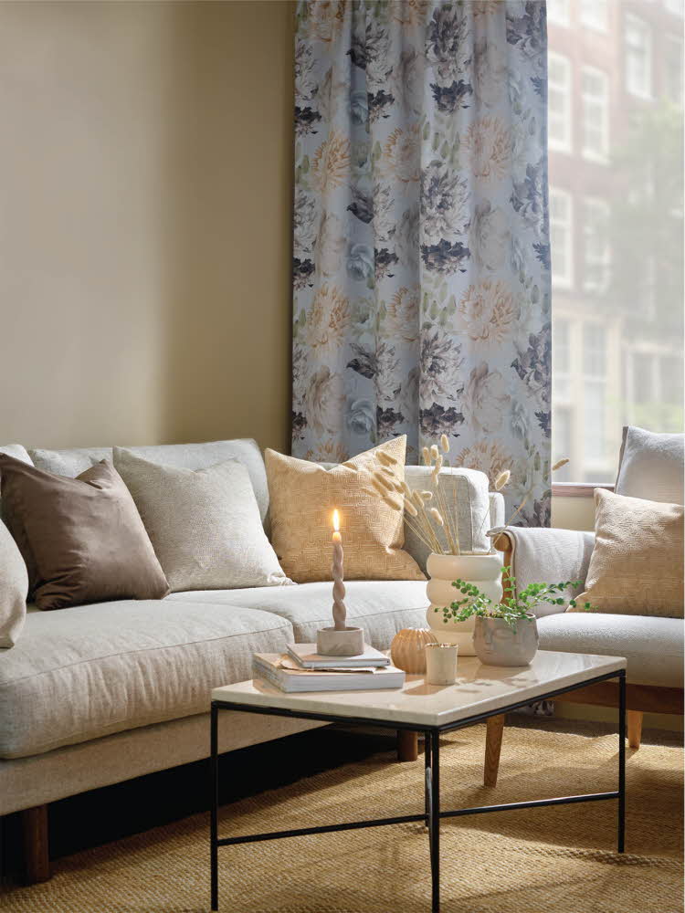 Lys sofa og et bord dekket med en vase med strå, grønn plante og tent lys