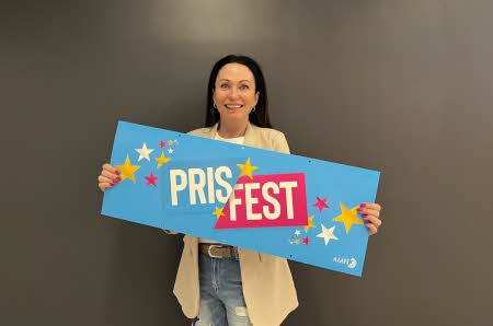 En dame som smiler og holder en Prisfest-plakat