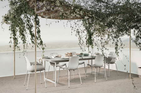 Utendørs spisestue med grått spisebord og stoler. Natur pergola.
