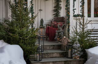 Inngang til et hus dekorert til jul med et juletre og julenisser plassert på trappen.