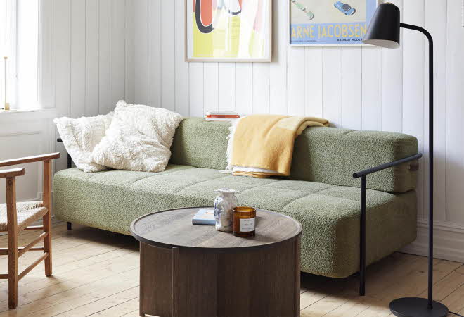 En stue med en grønn sofa, en lenestol, et stuebord og en gulvlampe