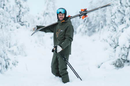Mann holder aplinski over høyre skulder og er kledd i grønn vinterjakke og grønn skibukse