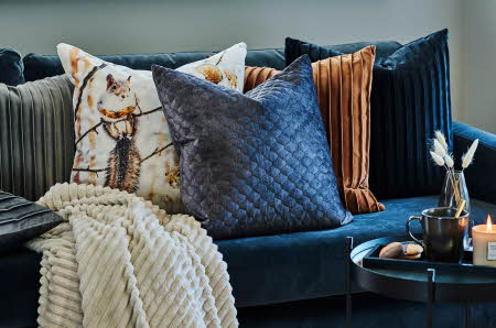 En blå sofa med fem pynteputer i forskjellig farge og tekstur på