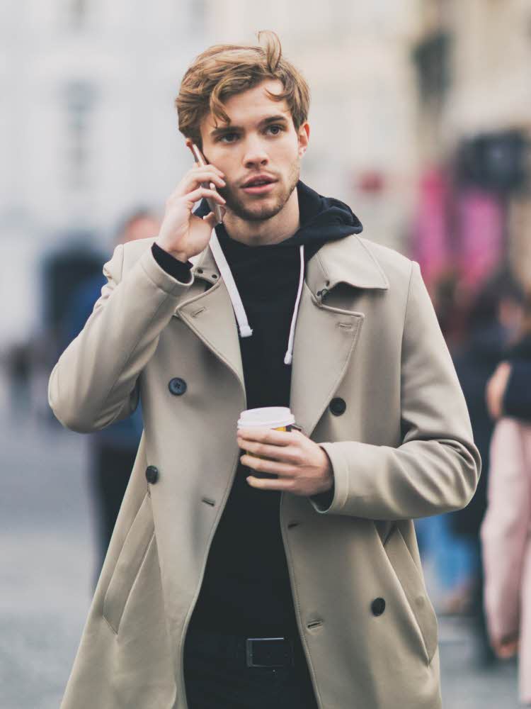 Mann kledd i sort hettegenser og beige frakk.