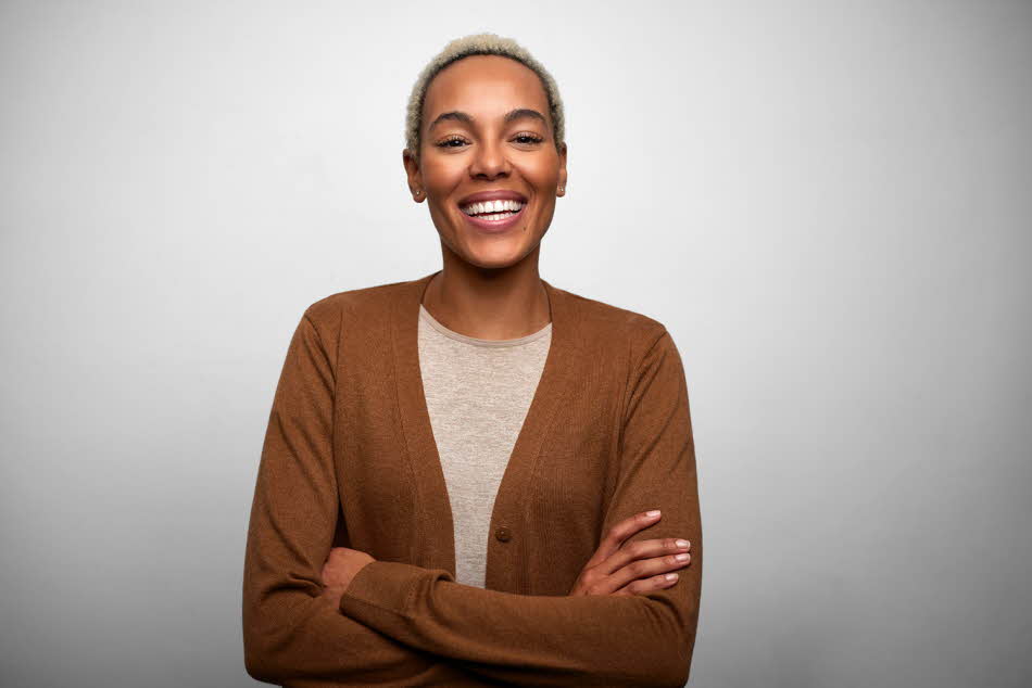 En dame med brun cardigan står foran en grå vegg og smiler