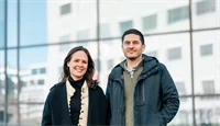 Madelenè Jespersen og Georgios Skouroliakos poserer utendørs i vinterjakker foran en glassfasade