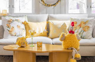 Et sofabord i tre med påskepynt og en beige sofa med påske puter