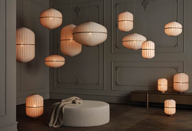 Mørk vegg med mange hengende lamper i varme toner og en rund puff.