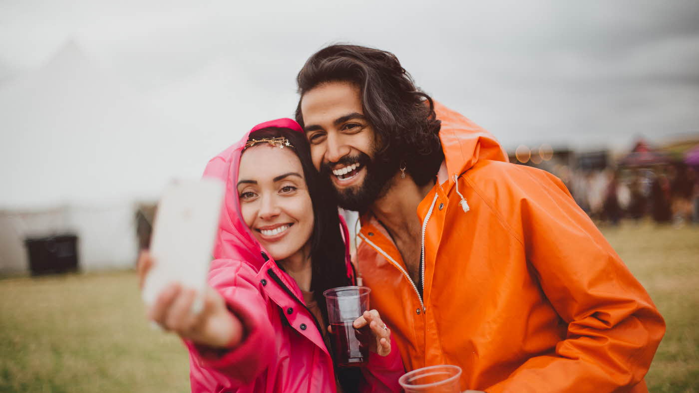 Dame og mann tar bilde av seg selv i ført rosa og oransje regnjakker på festival
