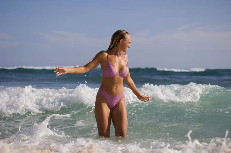 dame i rosa bikini som står i vannet på stranden
